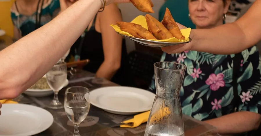 Um prato de croquetes fritos a ser passado entre convidados numa mesa com um jarro de vinho