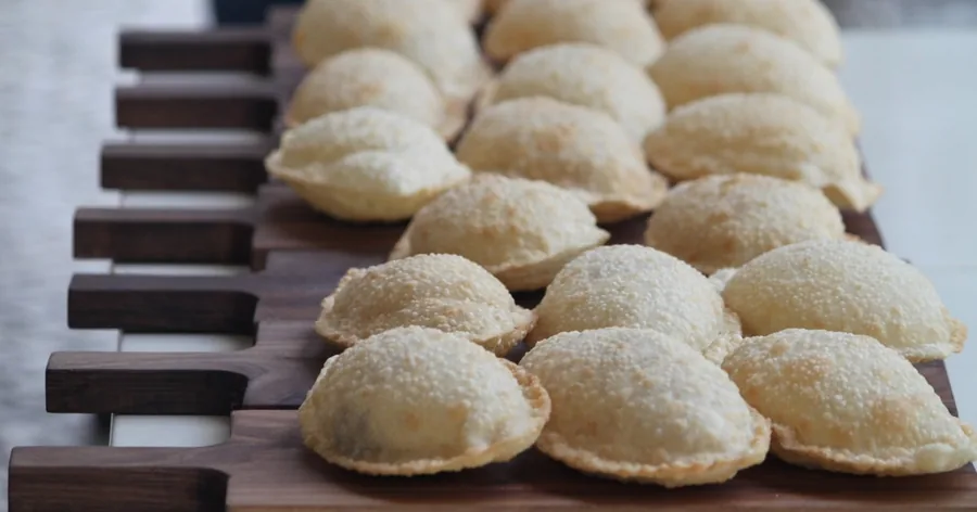 Meias-luas douradas de pastéis fritos alinhadas numa tábua de madeira escura