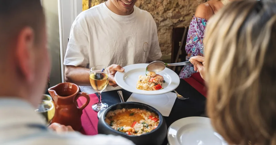 Uma mesa comprida de petiscos partilhados com pastéis de bacalhau, arroz e copos de vinho durante um passeio gastronómico